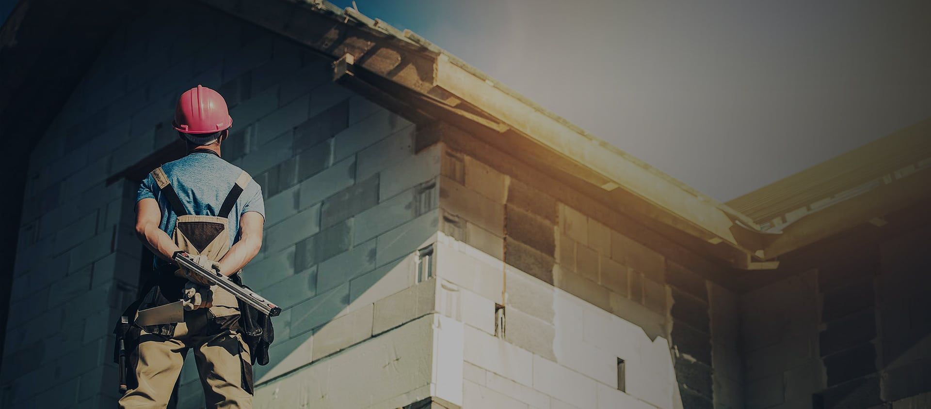 Construction worker in a hard hat stands looking at a building's corner.