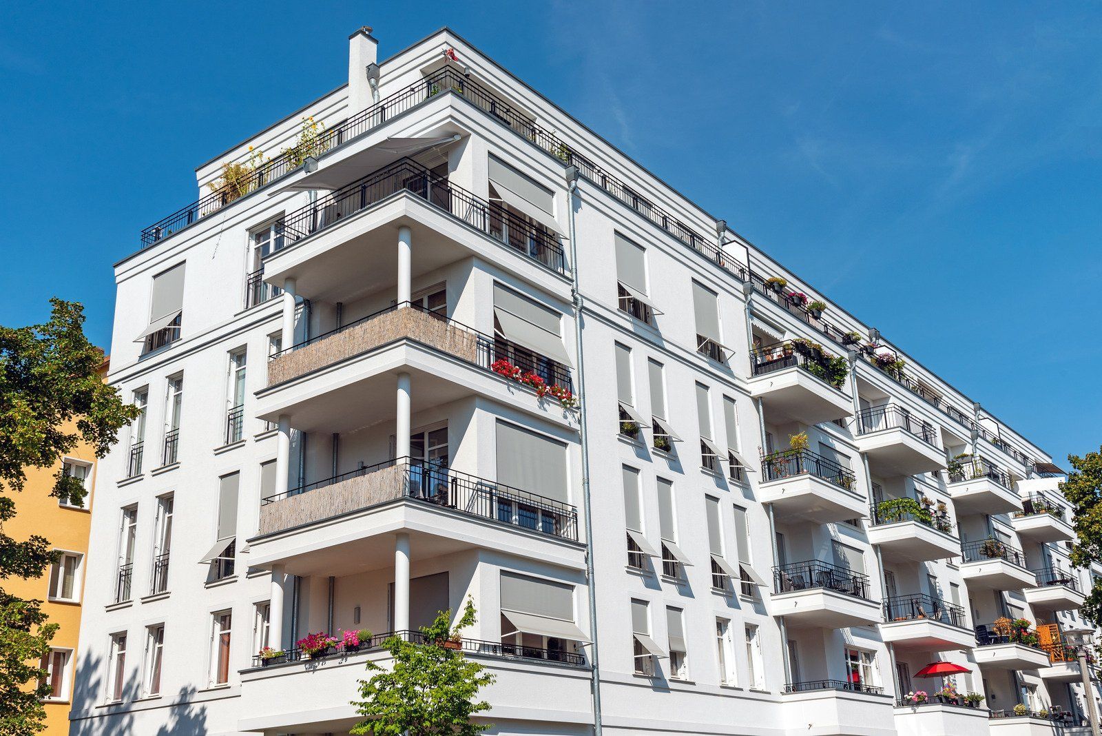 White multi-story apartment building with balconies, bright sunlight, blue sky.