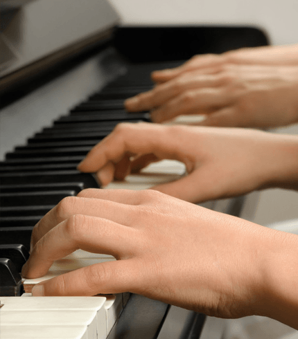 Four hands playing on the piano keys while the teacher gives the student a lesson