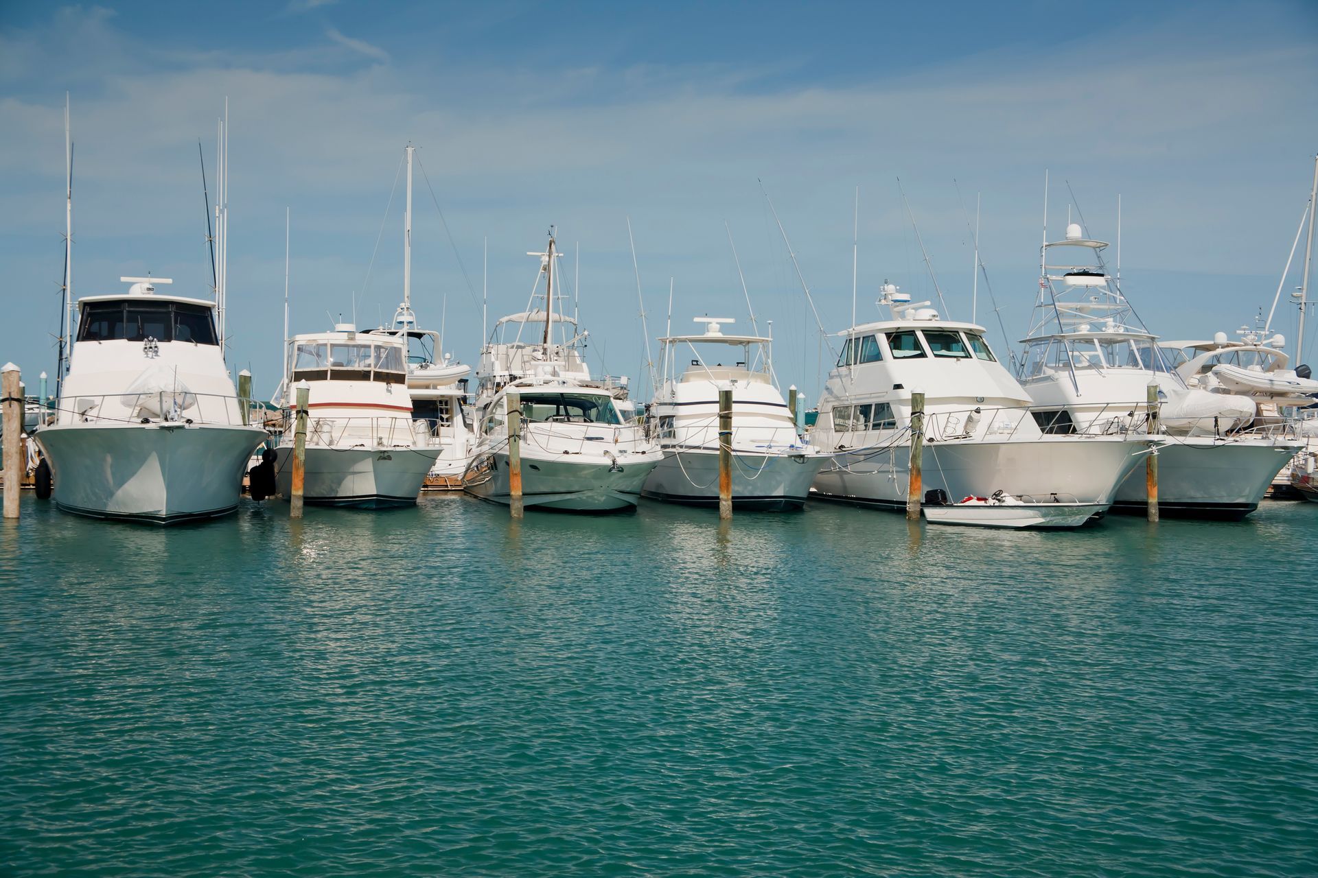 Boats docked at a marina in sunny weather, blue water, white boats, clear sky.