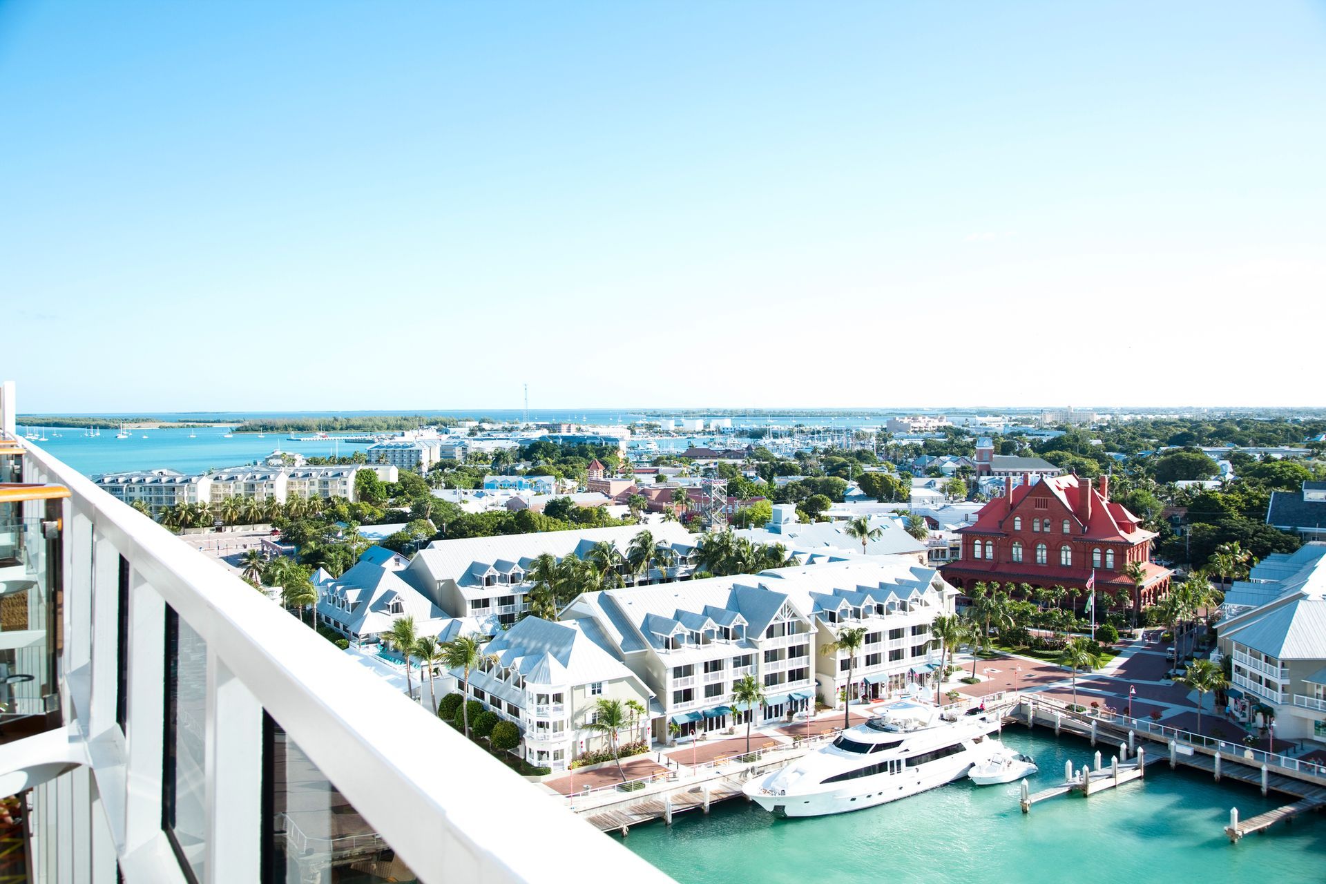 View of Key West, Florida, from a balcony, with buildings, boats, and turquoise water under a clear blue sky.