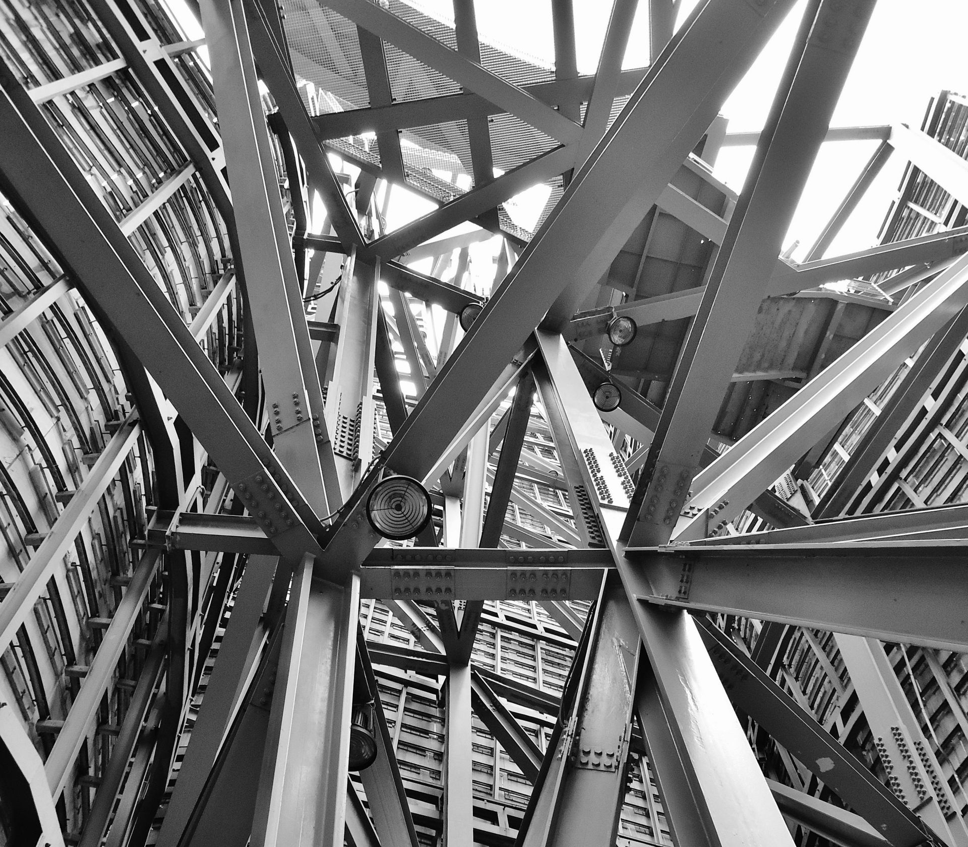 A complex network of steel beams and trusses, viewed from below, suggesting a tall structure's interior.