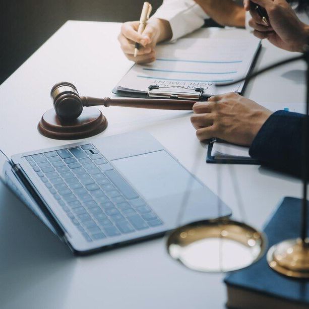 Law office with gavel, laptop, documents, and scales. People are writing.