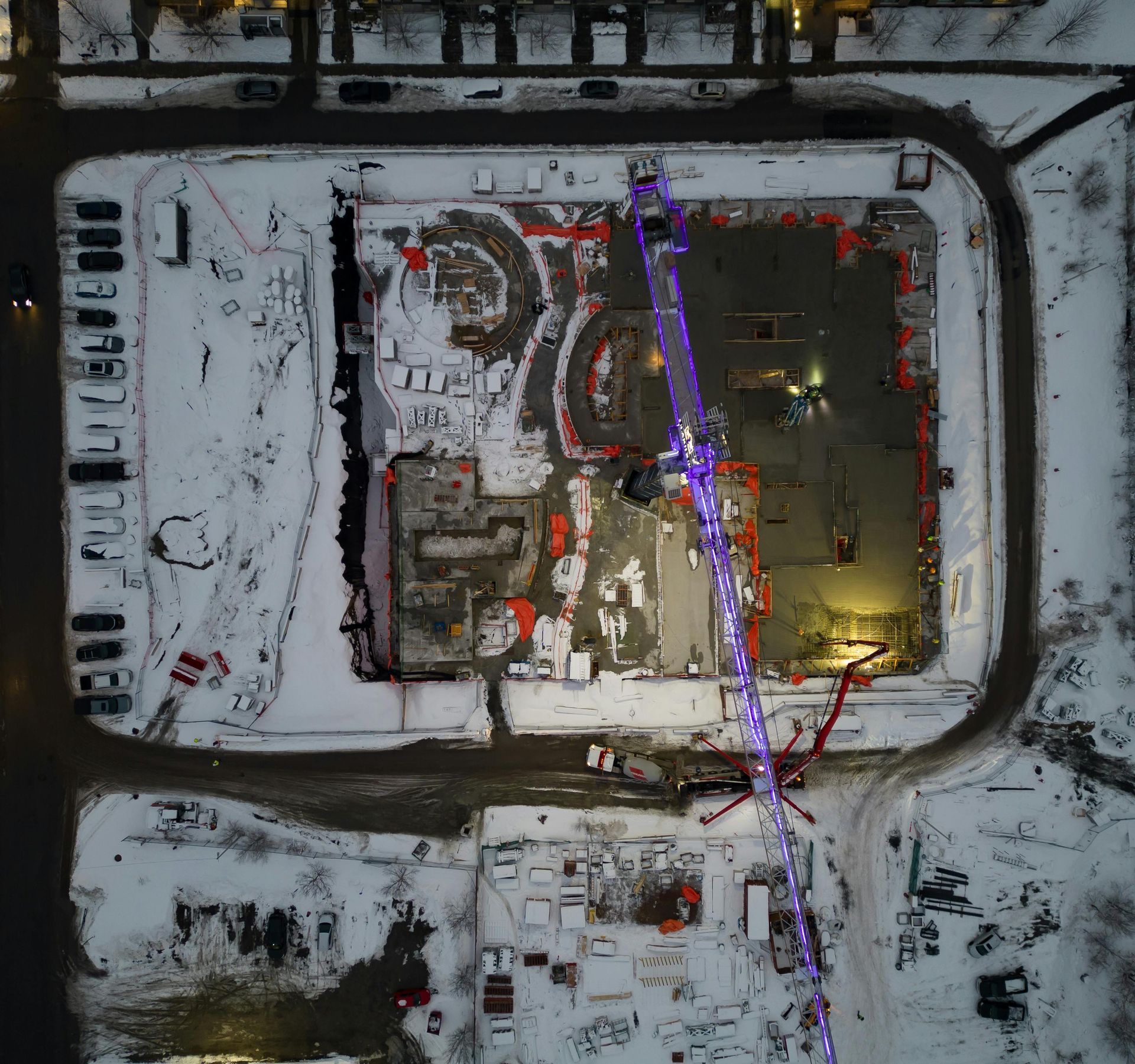 Aerial view of a snow-covered construction site with a large crane and concrete pouring equipment.