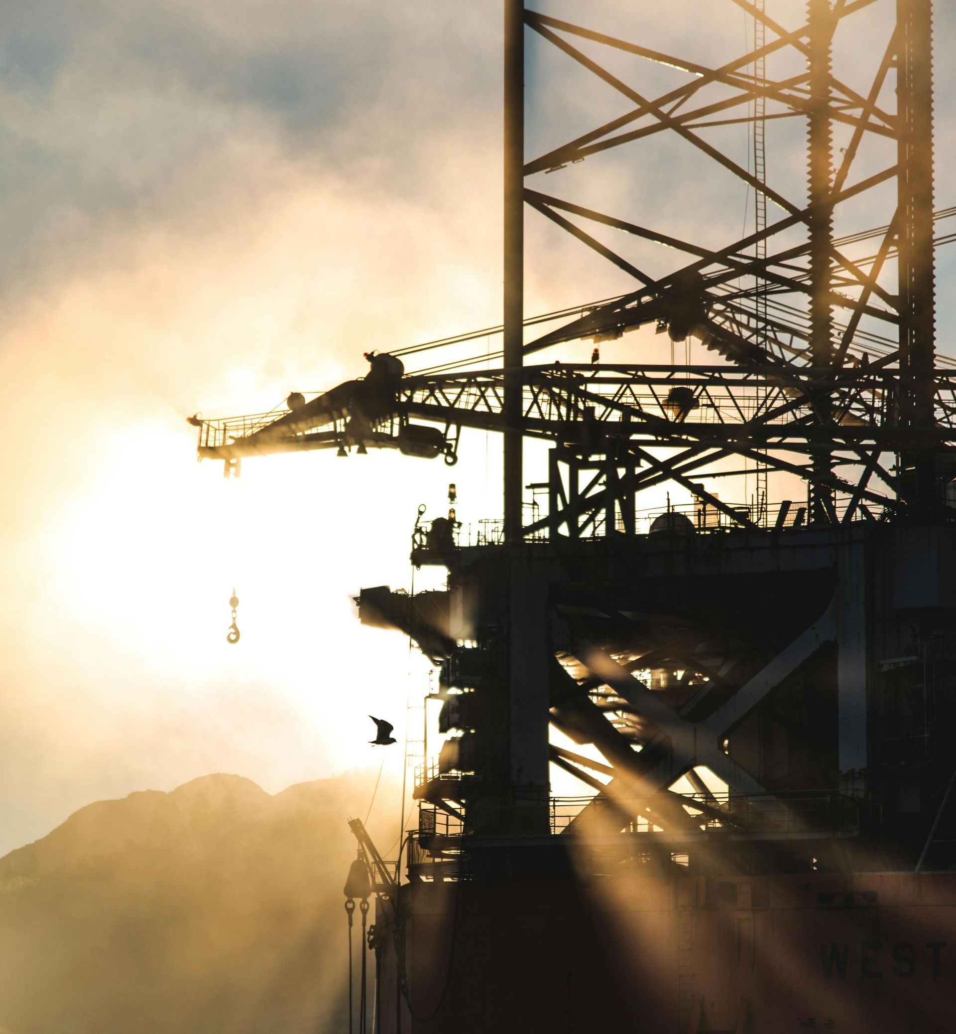Silhouette of a bridge under construction, sun shining through its structure.