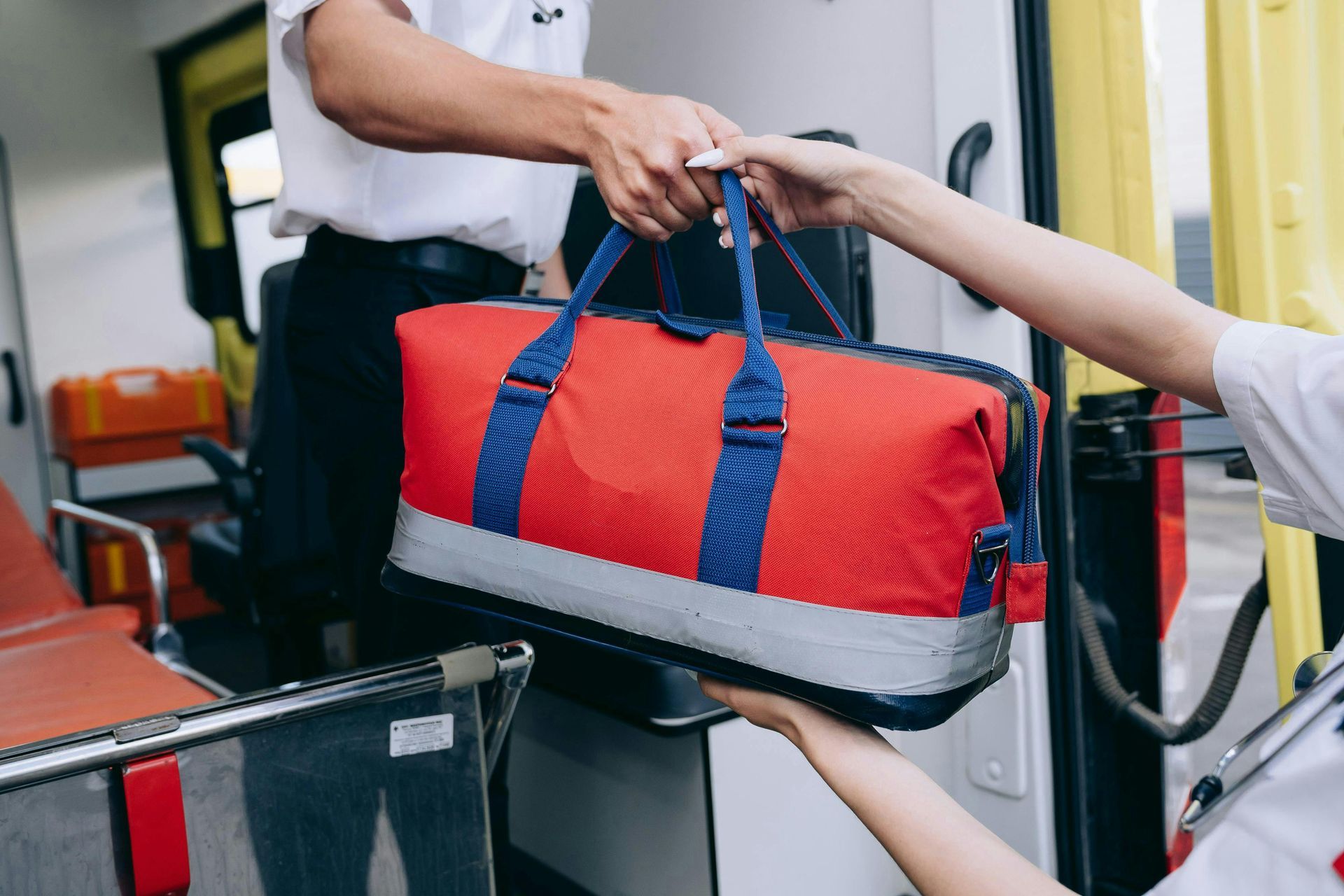 Emergency medical personnel exchanging a red and blue medical bag near an ambulance.