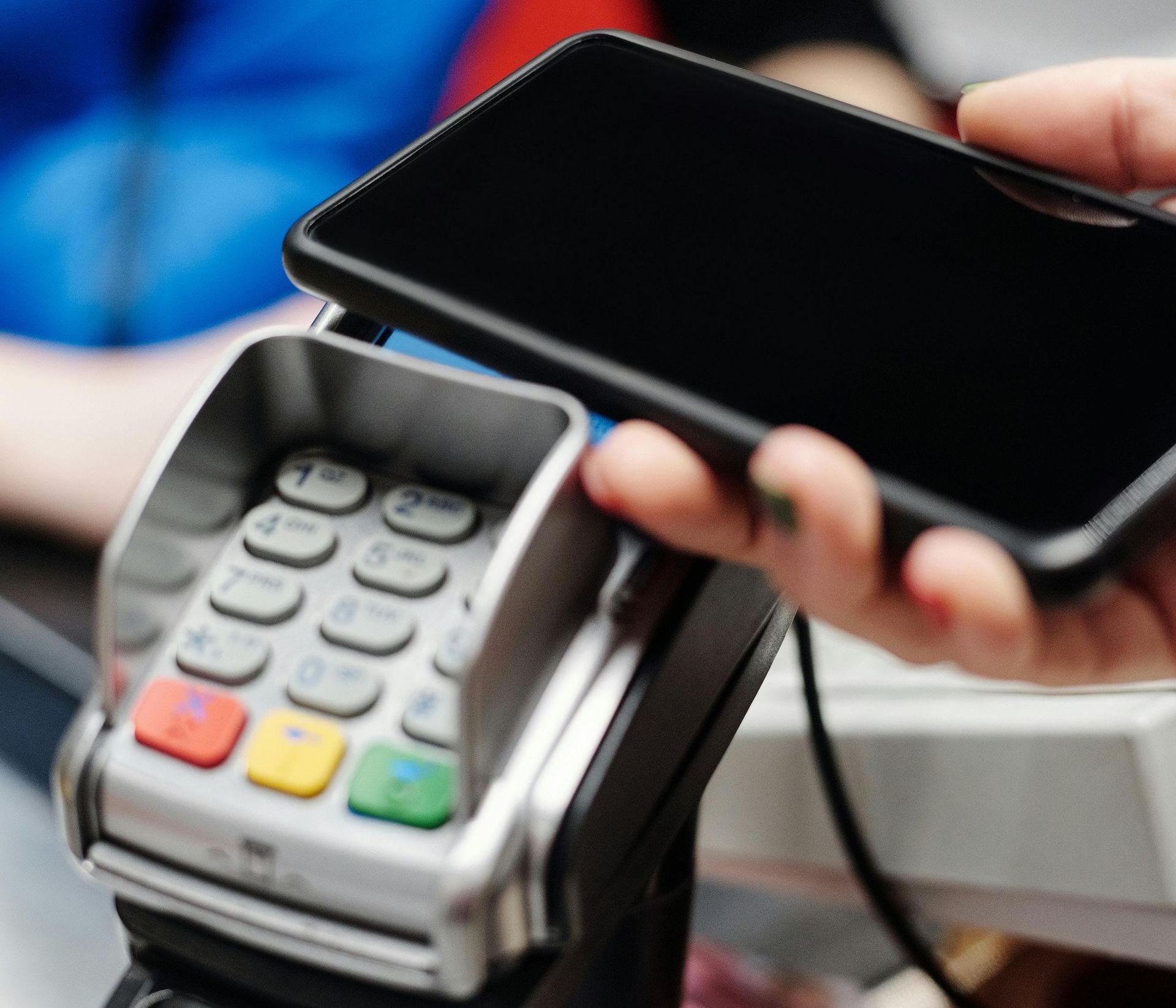 Person using a smartphone to make a contactless payment on a point-of-sale terminal.