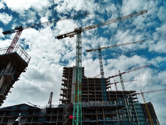 Construction site with multiple cranes working on a multi-story building under a cloudy sky.