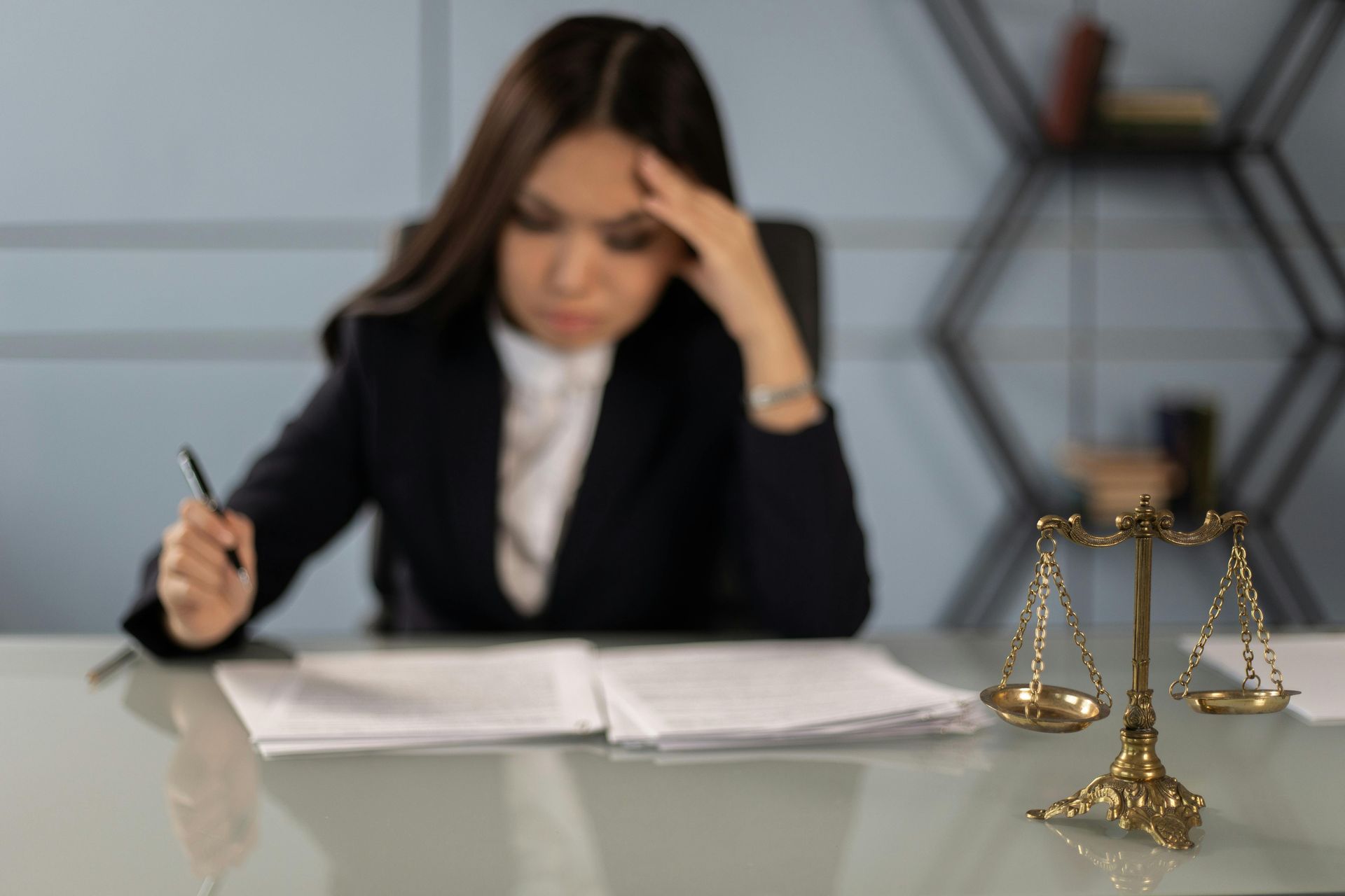 Woman in suit, focused on documents, scales of justice on desk.
