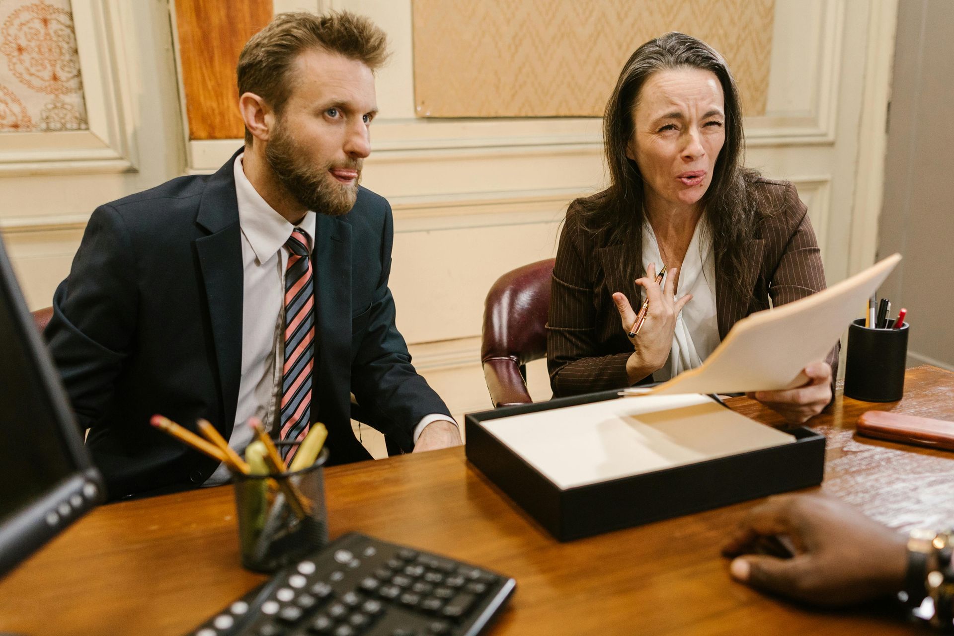 Man and woman at a desk look at paperwork. The woman gestures in disbelief, while the man looks concerned.