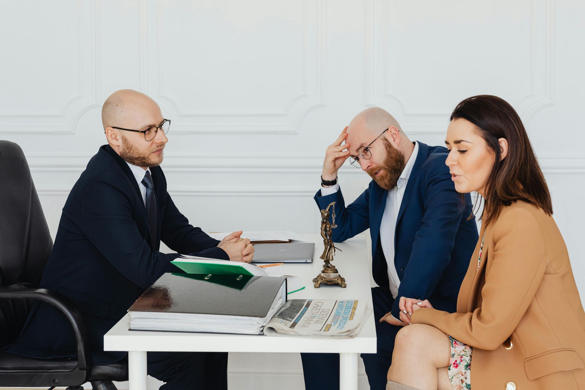 Lawyer advising a couple at a desk; man is stressed, woman is listening.