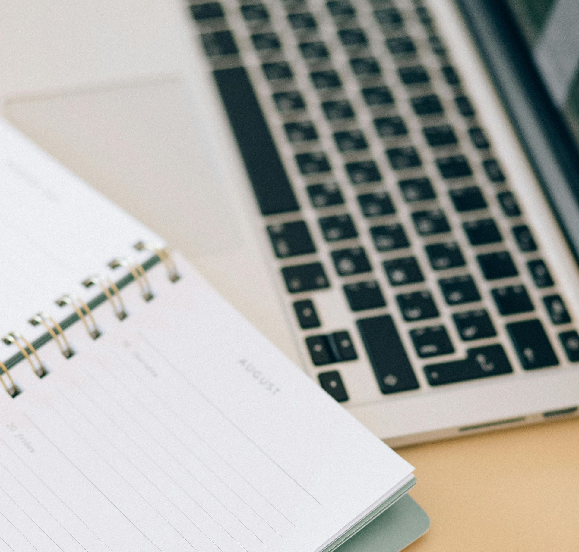 Open spiral notebook and laptop keyboard on a desk.