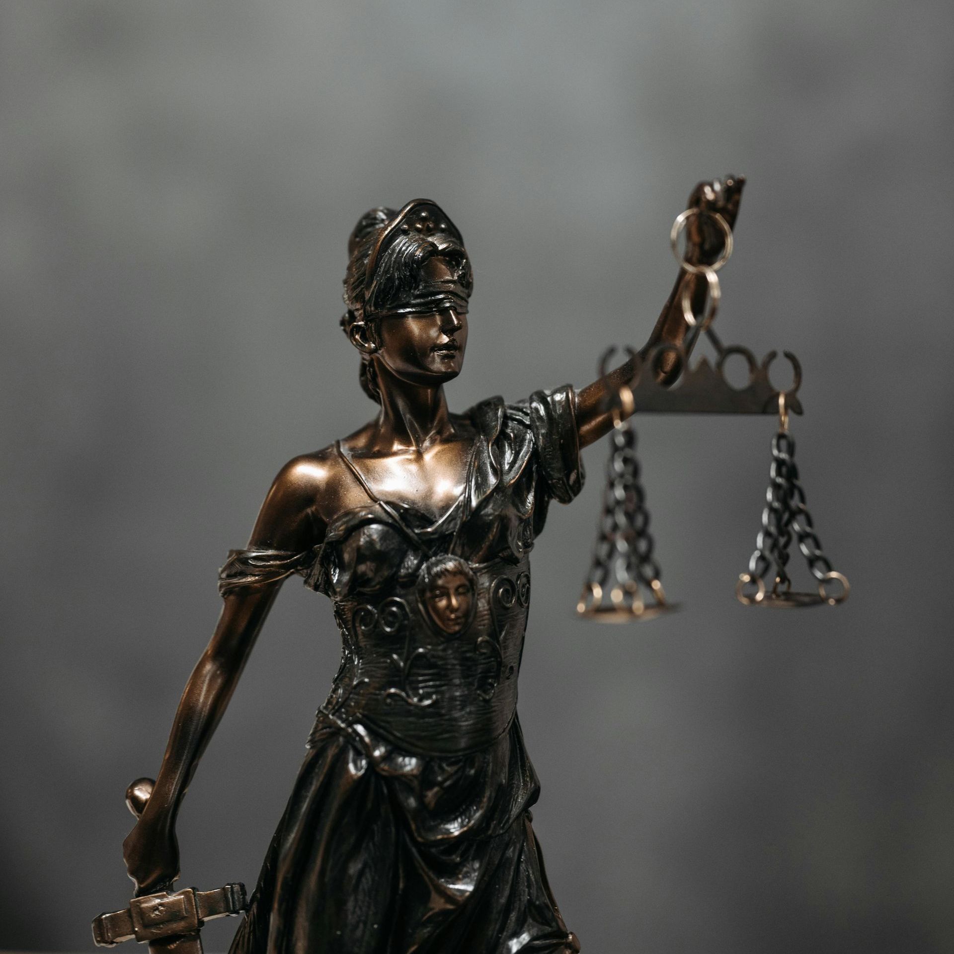 Statue of Lady Justice holding scales and sword, bronze finish, against a gray background.