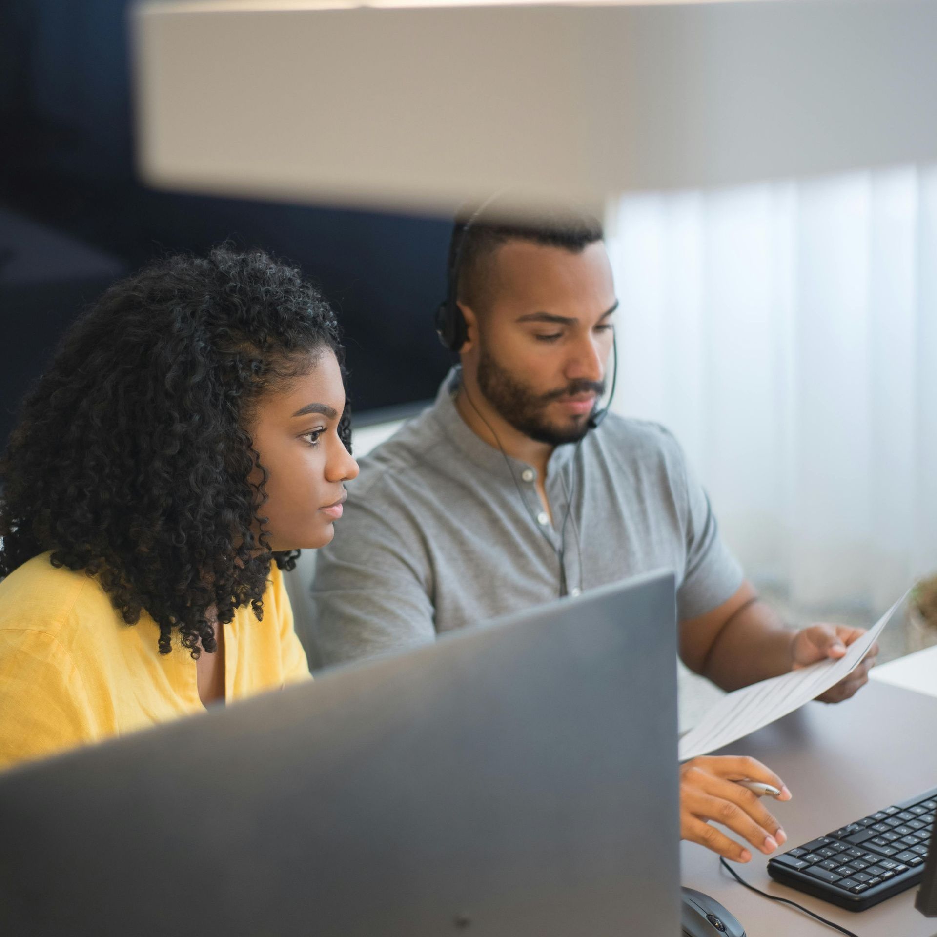 Woman and man reviewing documents at a computer, both looking focused in a well-lit office.