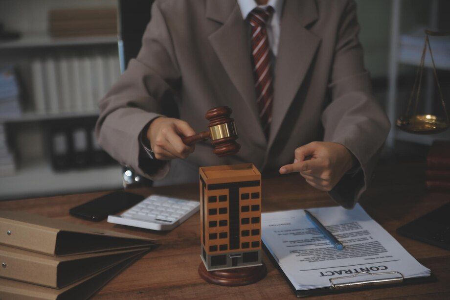 Lawyer holding gavel above a building model, pointing at it, with legal documents on the desk.