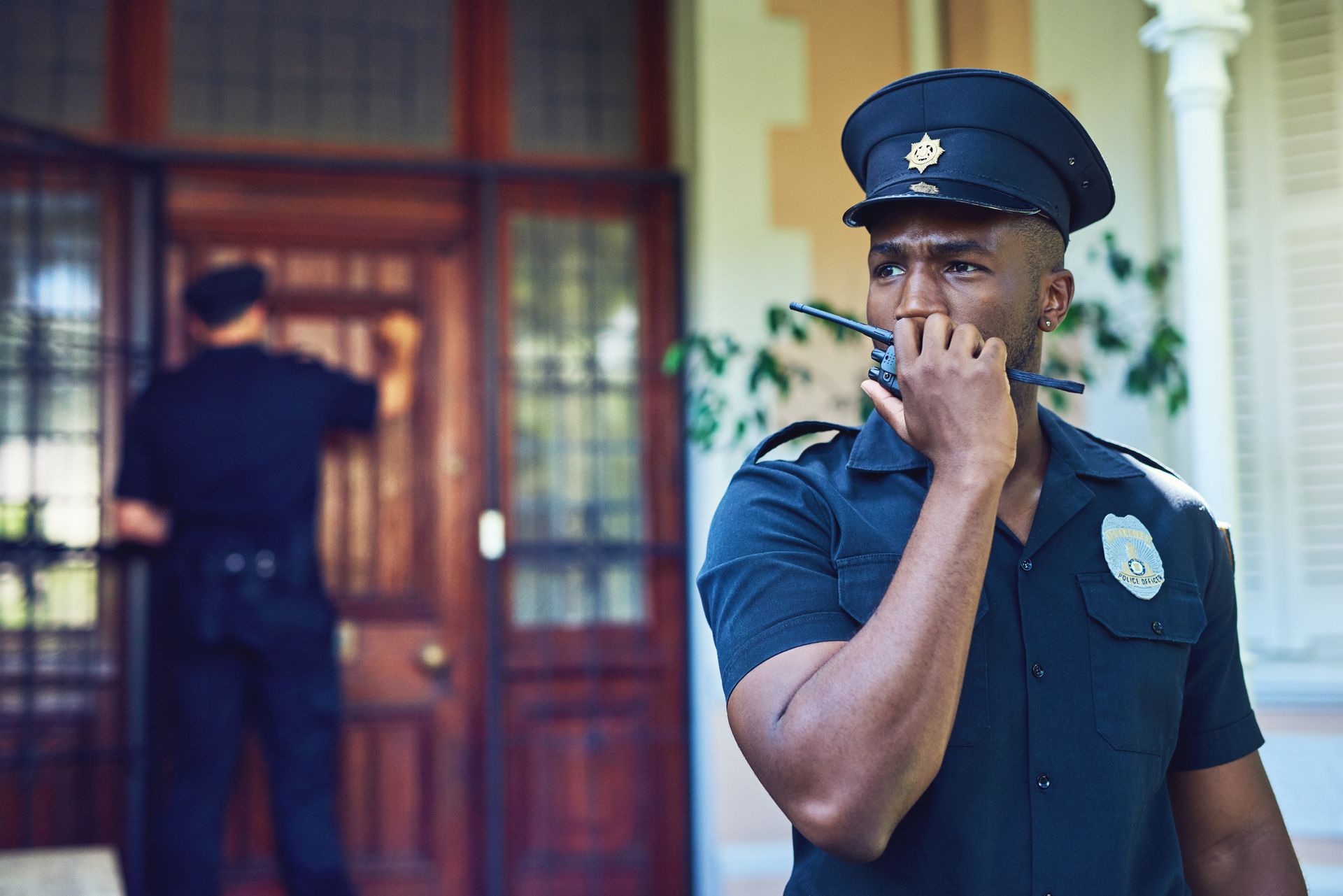 A security guard is talking on a walkie talkie in front of a door.