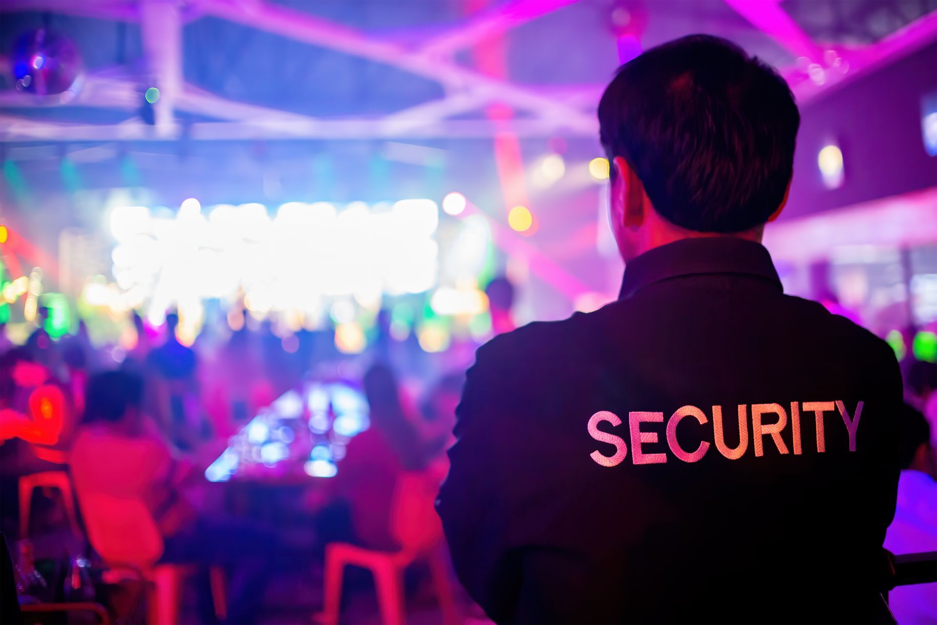 A security guard is standing in front of a crowd of people at a party.