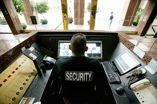 A security guard is sitting at a desk in front of a computer