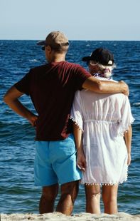 Two people standing arm in arm on a boat, facing the ocean under a clear sky.