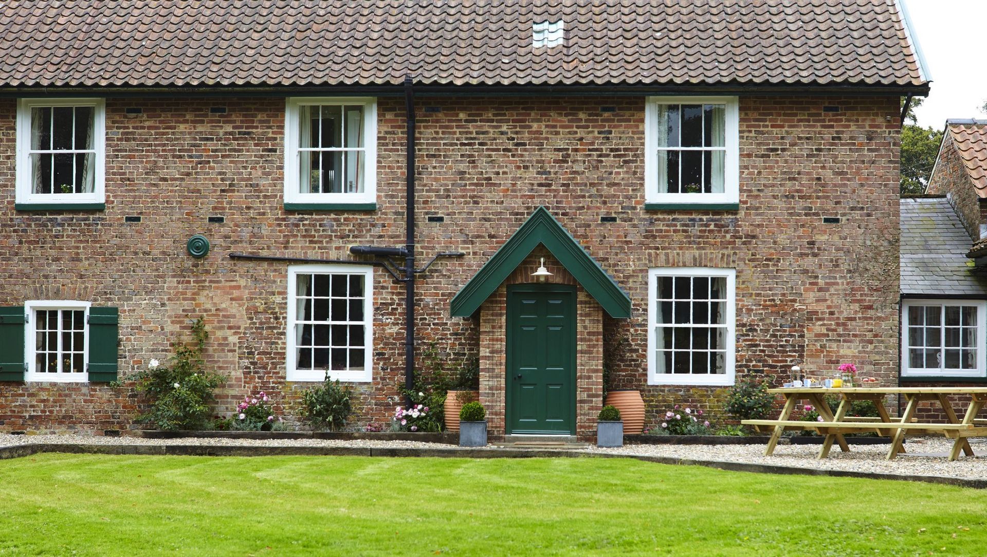 Brick cottage with green door and white windows, green lawn and picnic table.