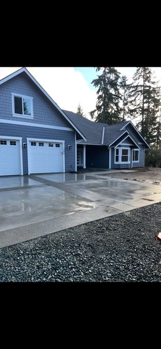 Blue-gray house with attached garage and wet concrete driveway beside gravel yard at dusk