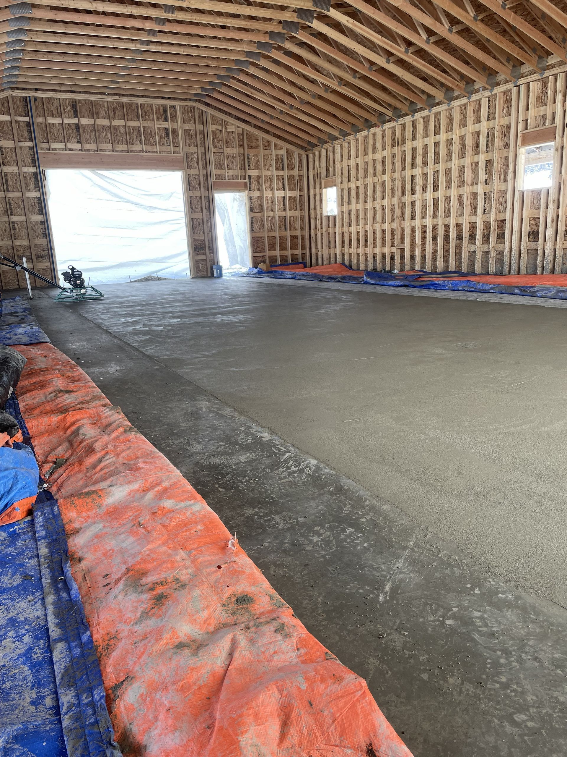 Interior of a wooden-framed building under construction with a freshly poured concrete floor.