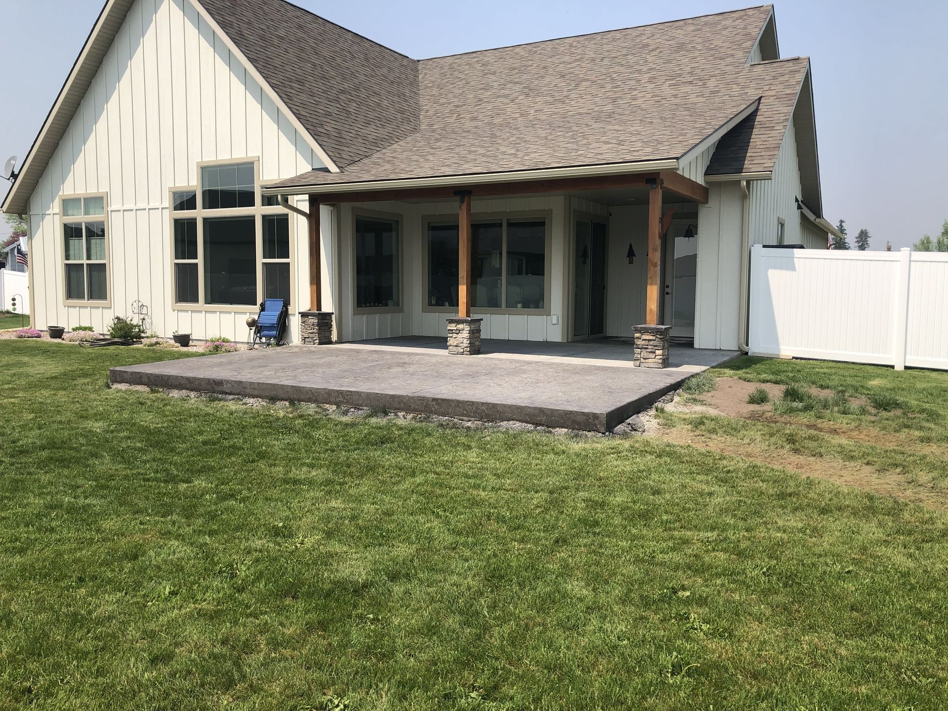 Suburban house with a large grassy backyard and small patio area, viewed from the rear