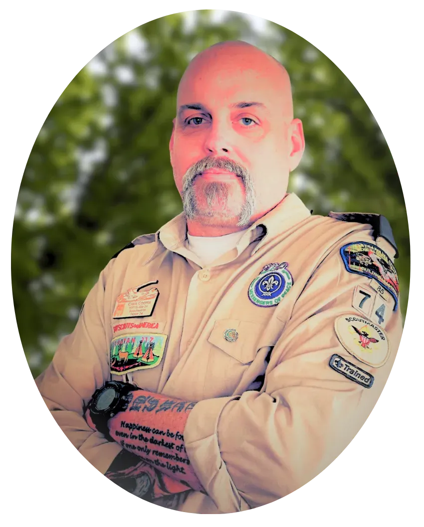 A person with a mustache, wearing a tan scout uniform with patches, 