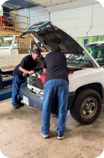 Two mechanics working on the engine of a white truck in a garage; hood up | Chip Ragans Auto, LLC