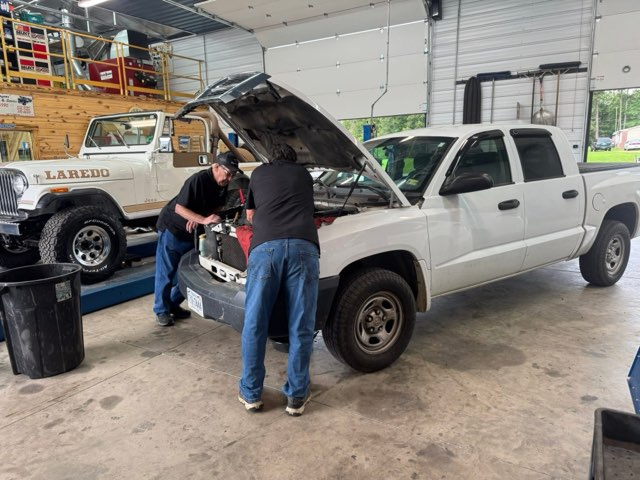 Two mechanics working on a white pickup truck with its hood open in a garage, a white Jeep next to it | Chip Ragans Auto, LLC