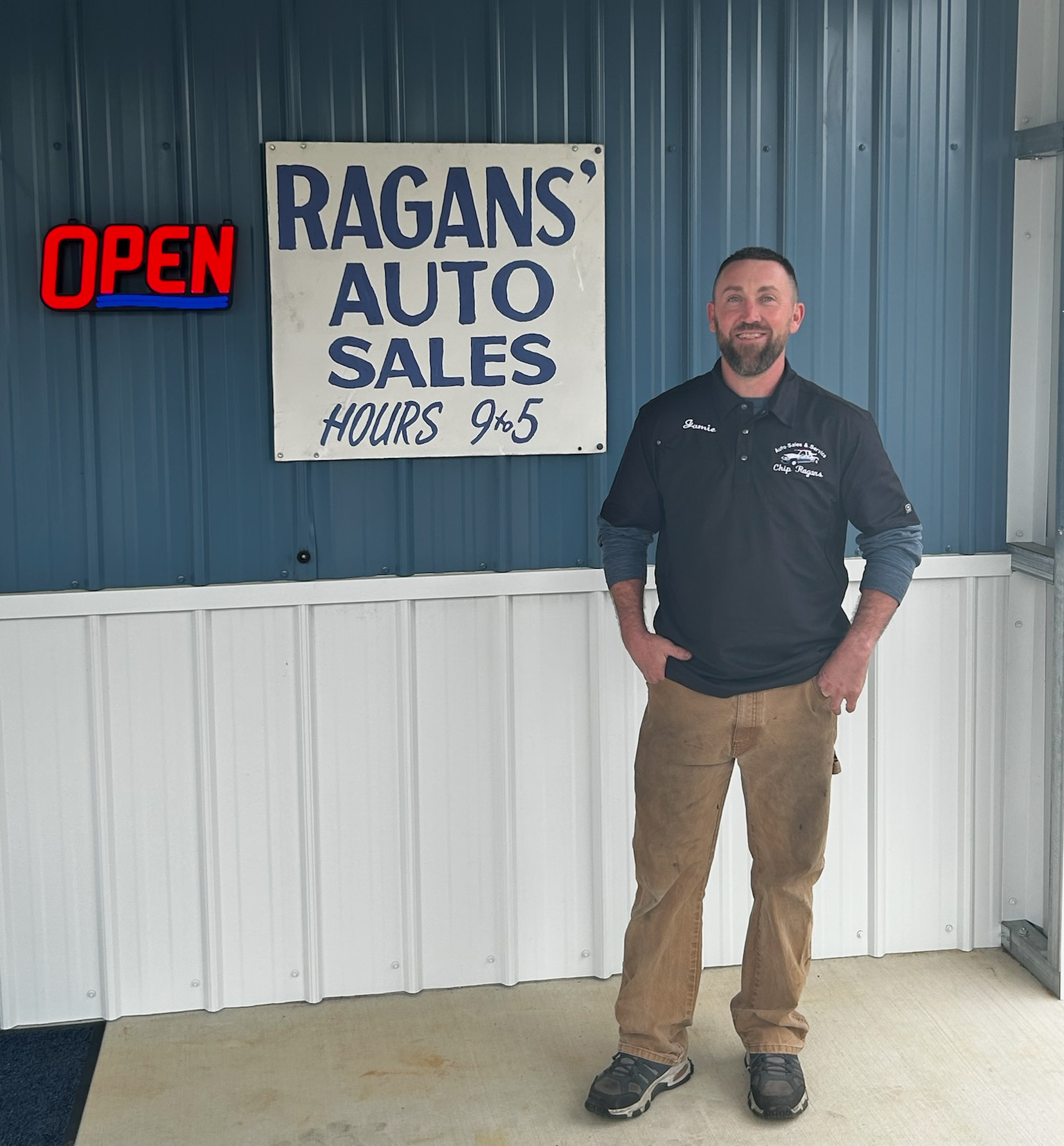 Man standing outside Ragan's Auto Sales, sign says 