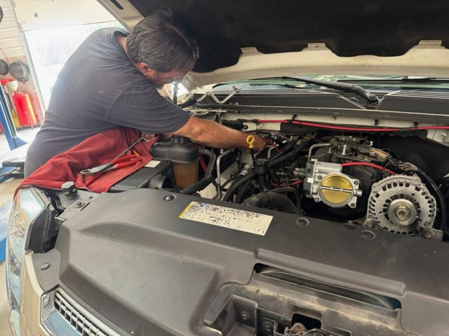 Mechanic working under the hood of a white vehicle in a shop; examining engine | Chip Ragans Auto, LLC