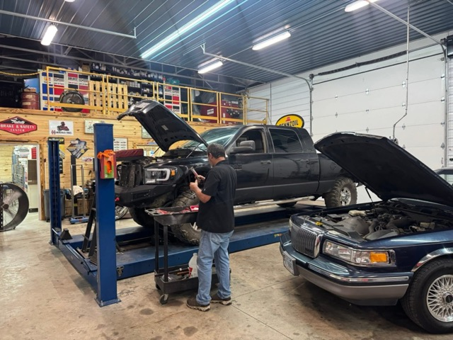Mechanic working on a black truck raised on a lift in a garage, another car nearby | Chip Ragans Auto, LLC