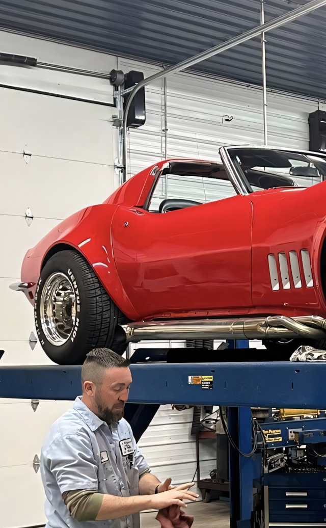 Man wiping hands in a garage with a red convertible Corvette on a lift | Chip Ragans Auto, LLC