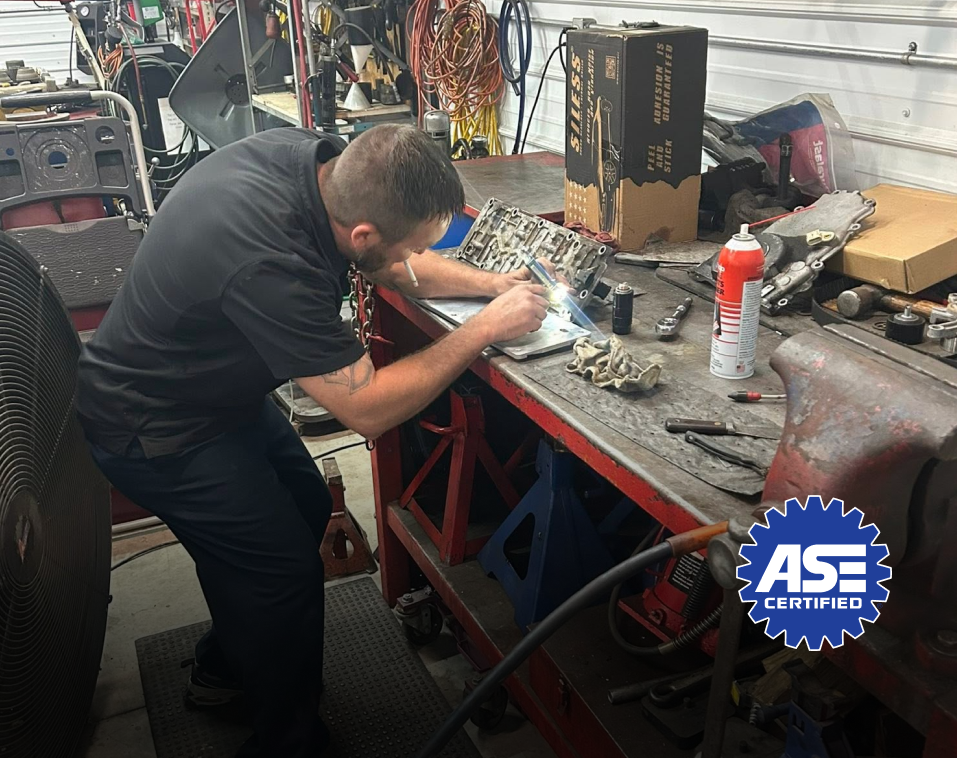 Mechanic working on parts at a workbench in a cluttered shop; ASE Certified logo | Chip Ragans Auto, LLC