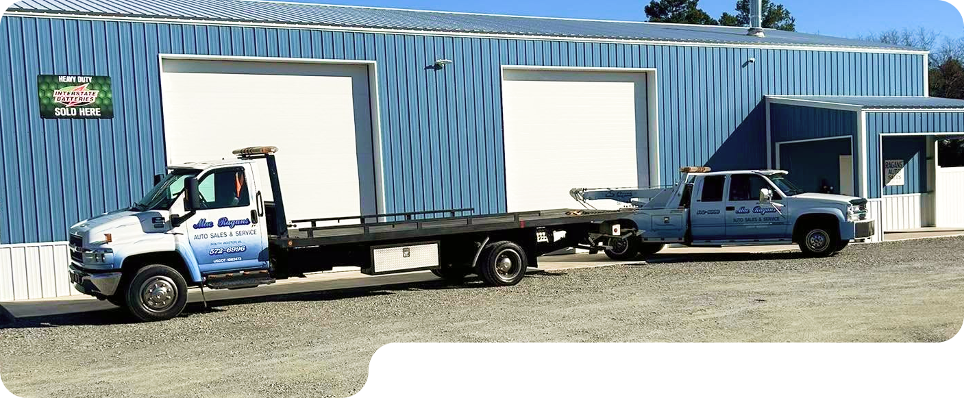 White tow truck, with blue gradient, parked in front of a metal building.  