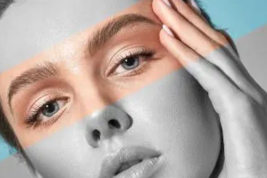 Close-up of a woman's face with light skin. Partially shaded in gray. Hand on forehead. Blue eyes and full lips.