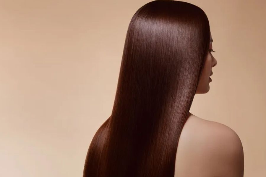 Woman with long, shiny, straight brown hair against a light brown backdrop.