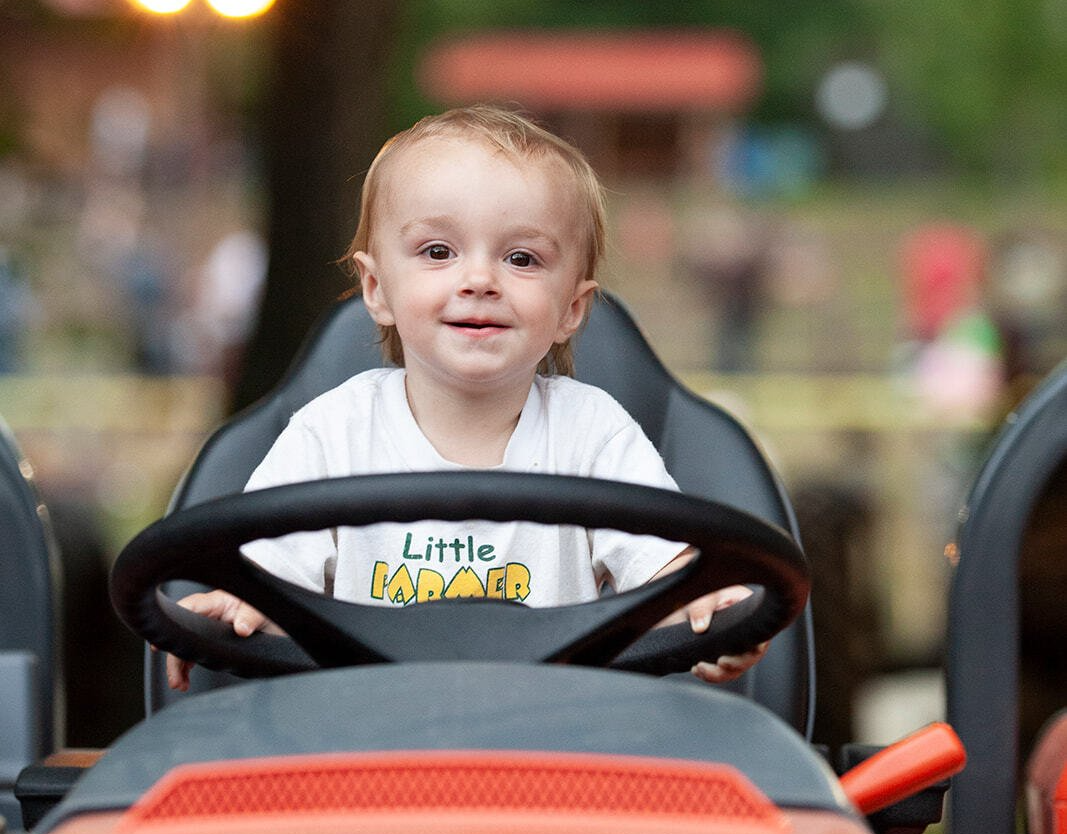 A little boy wearing a little man shirt is driving a go kart