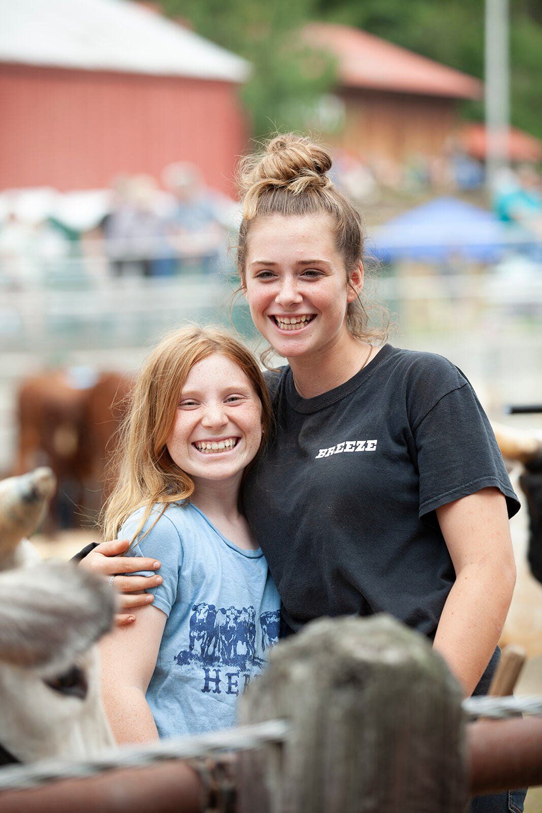 Two young girls are posing for a picture in front of a fence.
