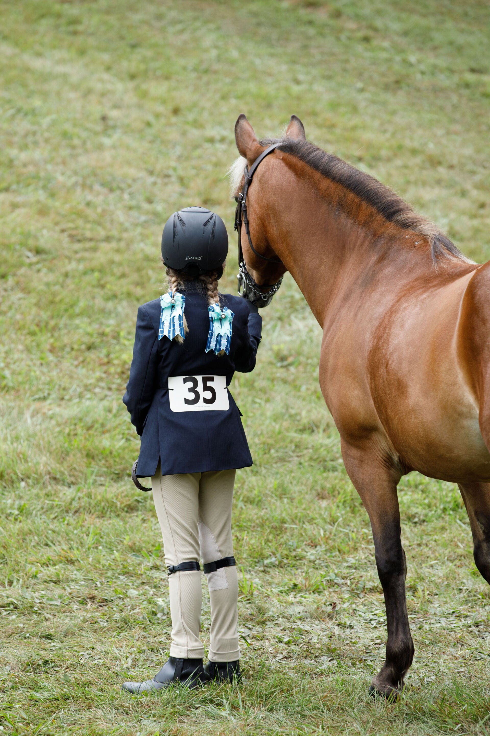 A young girl is standing next to a brown horse in a field.