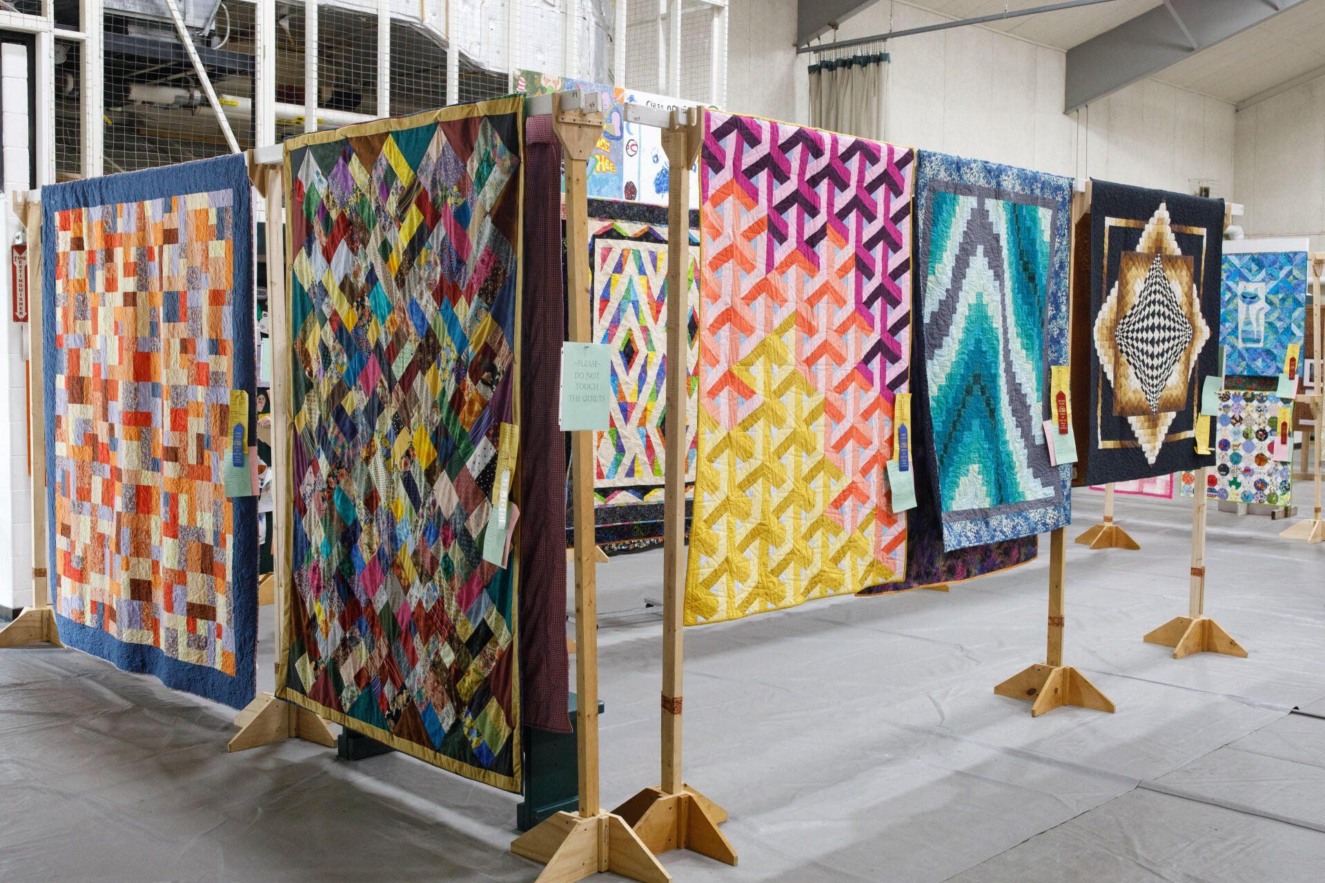 A row of colorful quilts are hanging on wooden racks.