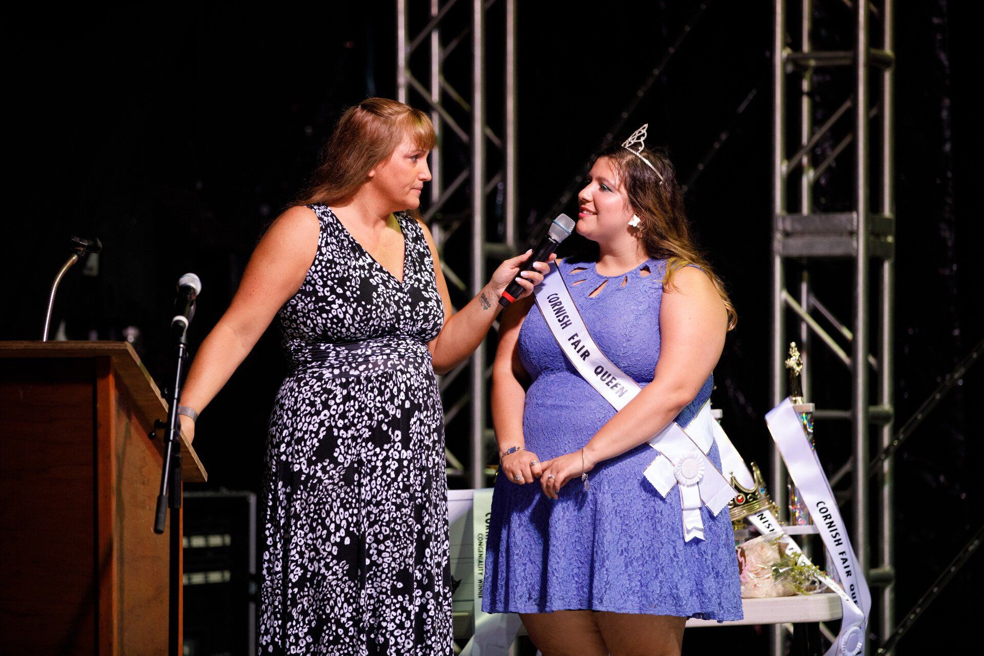 Two women are standing next to each other on a stage talking into microphones.