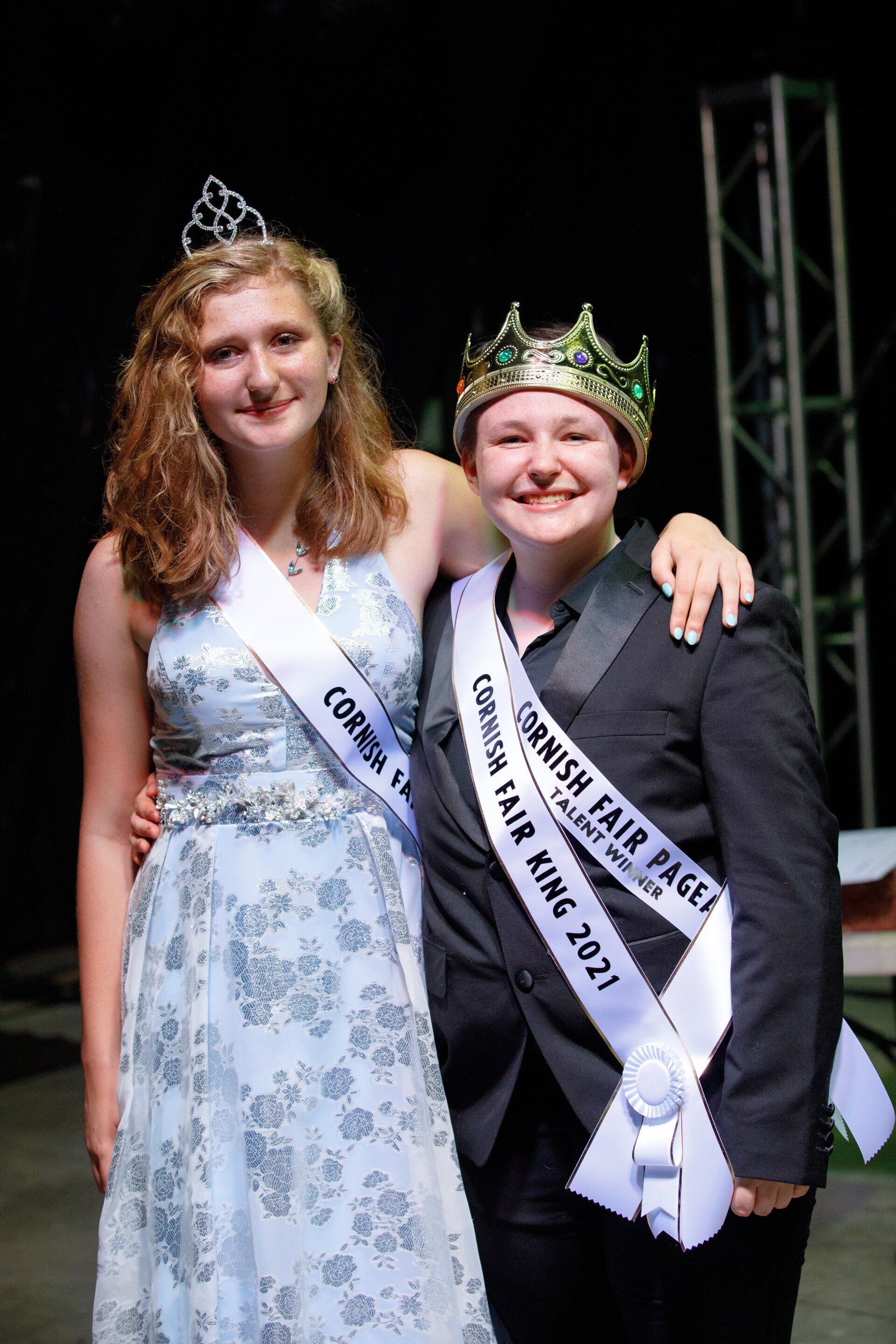 A man and a woman wearing crowns and sashes are posing for a picture.