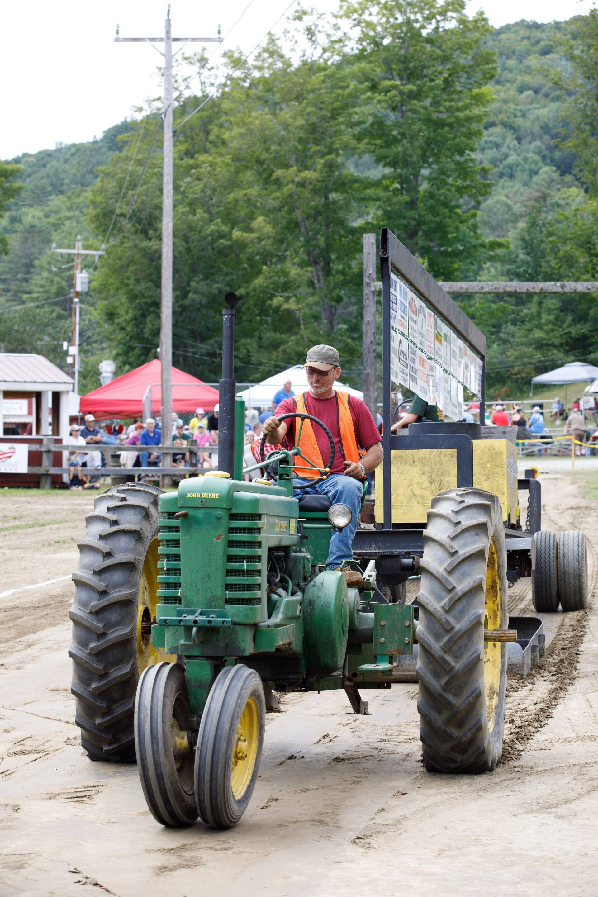 A man is driving a john deere tractor on a dirt road
