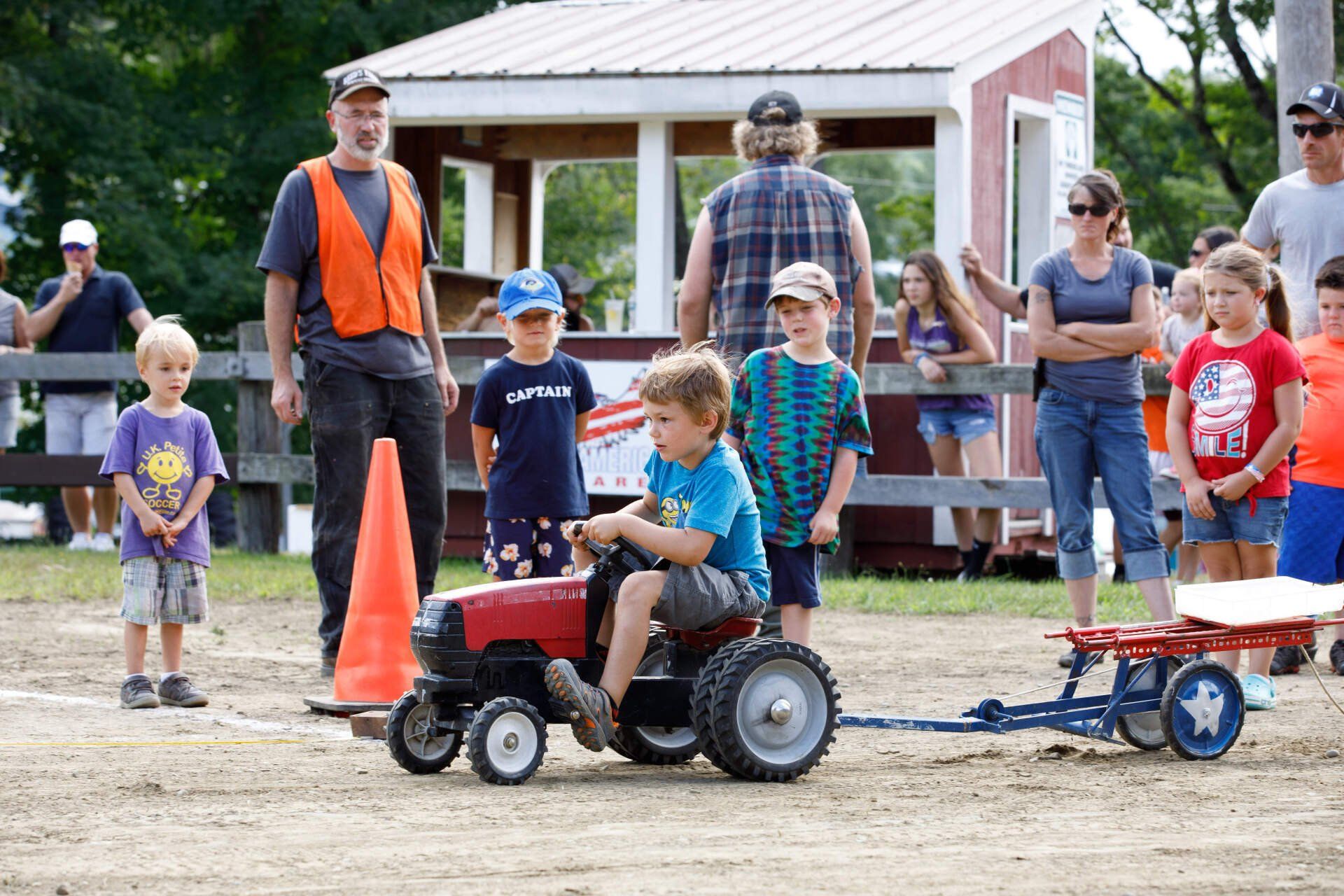 A boy is riding a toy tractor with a wagon attached to it.