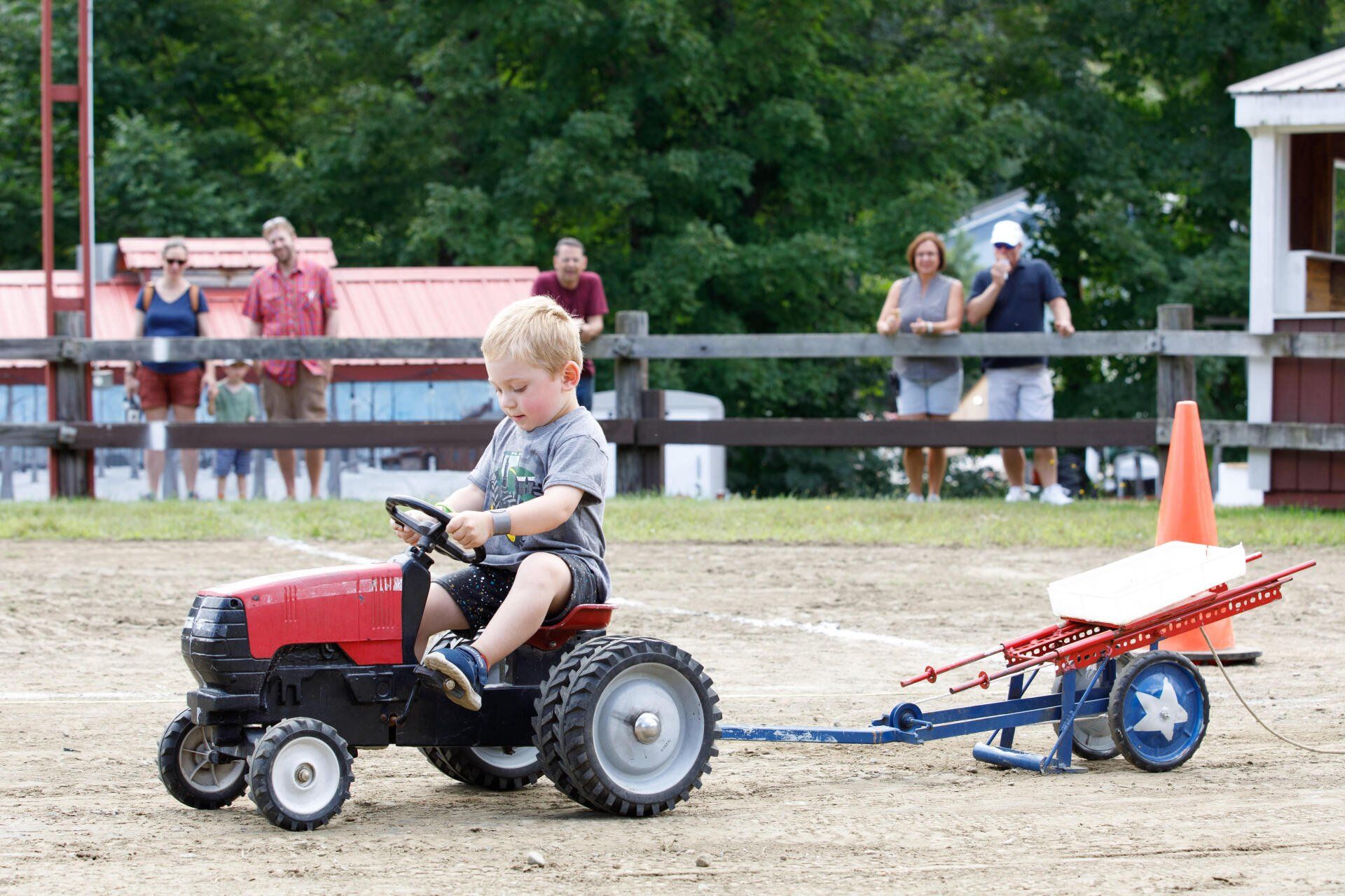 A young boy is riding a toy tractor pulling a wagon.