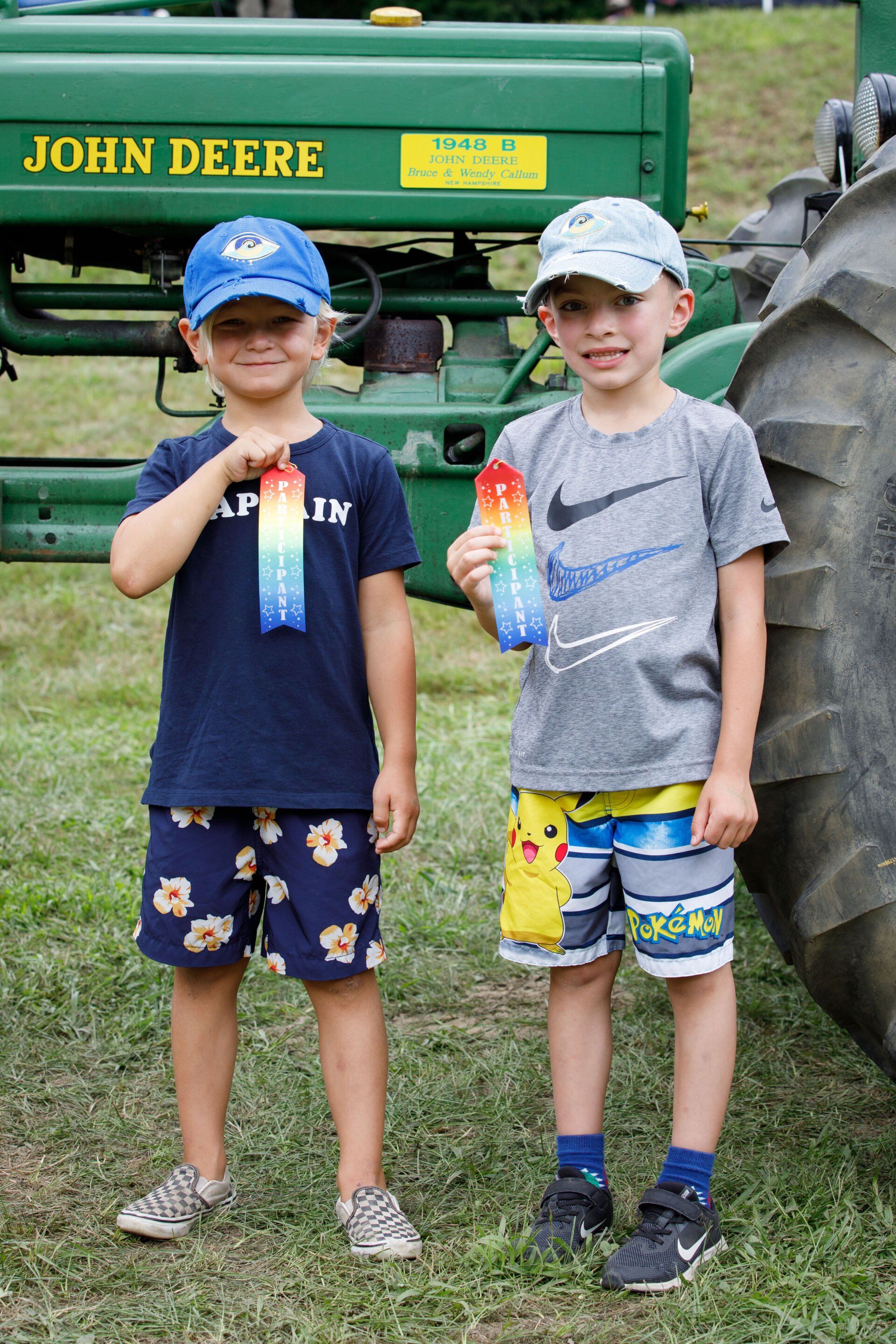 Two young boys are standing next to each other in front of a john deere tractor.