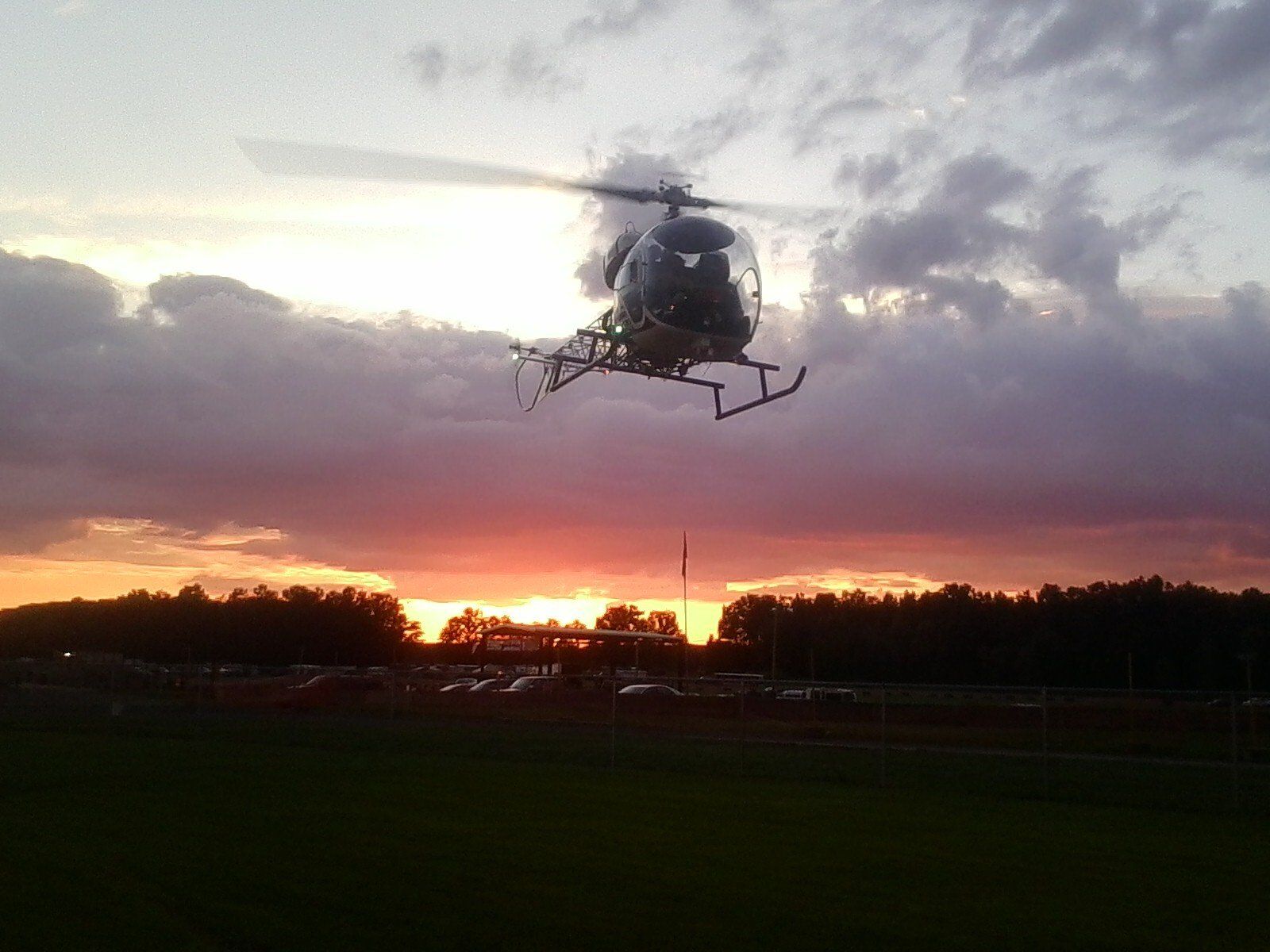 A helicopter is flying over a field at sunset