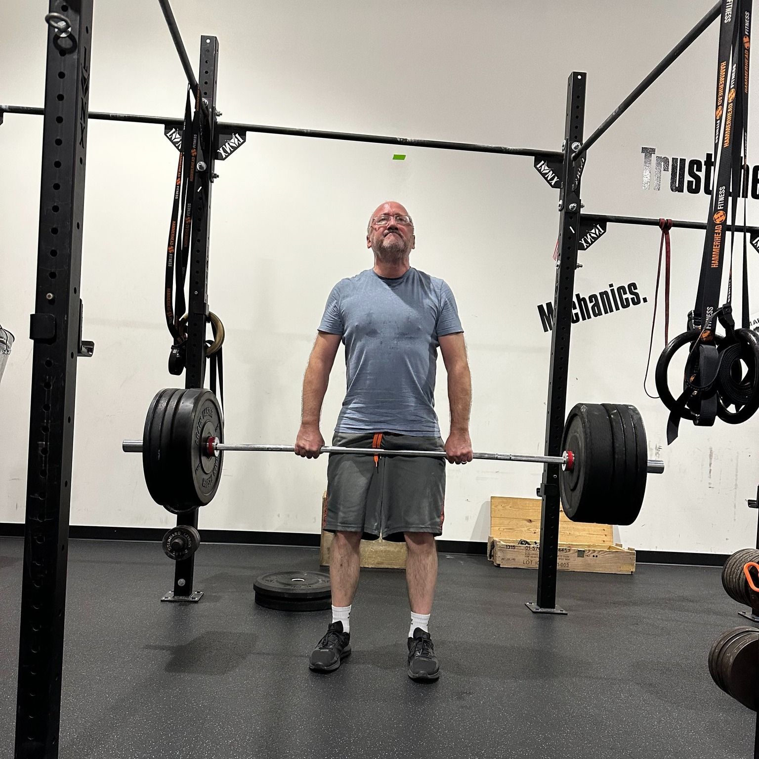 People exercising with weights in a gym. Some seated, some standing. A coach observes the workout.
